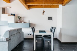 Zona pranzo moderna con tavolo bianco e sedie nere, un divano grigio e un soffitto in legno.