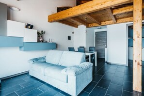 Un soggiorno moderno con un divano chiaro, un soffitto in legno e un pavimento piastrellato scuro.