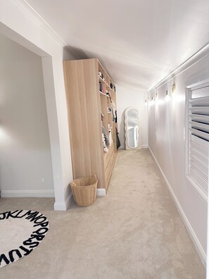 A hallway with a wooden wardrobe, a white wall, a white door, and a light fixture.