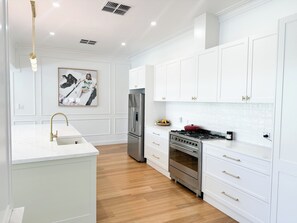 A modern kitchen with white cabinetry, stainless steel appliances, and a marble countertop.
