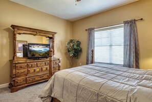 A bedroom with a wooden dresser, a television, a large bed, and a window with curtains. - Mountains View Condo, Pool Access, WIFI (Pigeon Forge)