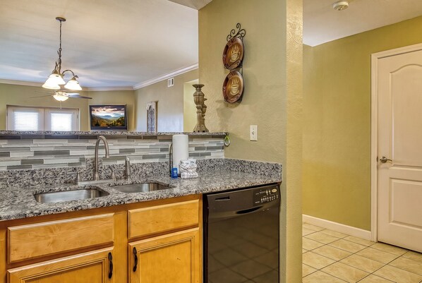 A kitchen with granite countertops, a dishwasher, wooden cabinets, a ceiling fan, and a wall-mounted television. - Mountains View Condo, Pool Access, WIFI (Pigeon Forge)