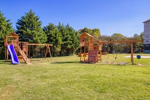 A playground with a slide and swings, surrounded by grass and trees. - Mountains View Condo, Pool Access, WIFI (Pigeon Forge)