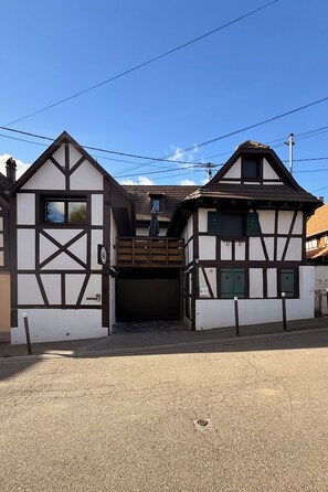 A traditional half-timbered building with a garage entrance, a visible chimney, and a clear sky. - New Listing (Breuschwickersheim)