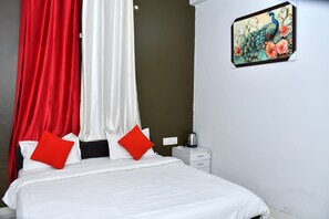 Une chambre d’hôtel avec un lit, des rideaux rouges et blancs, une table de chevet avec une bouilloire et un tableau au mur.