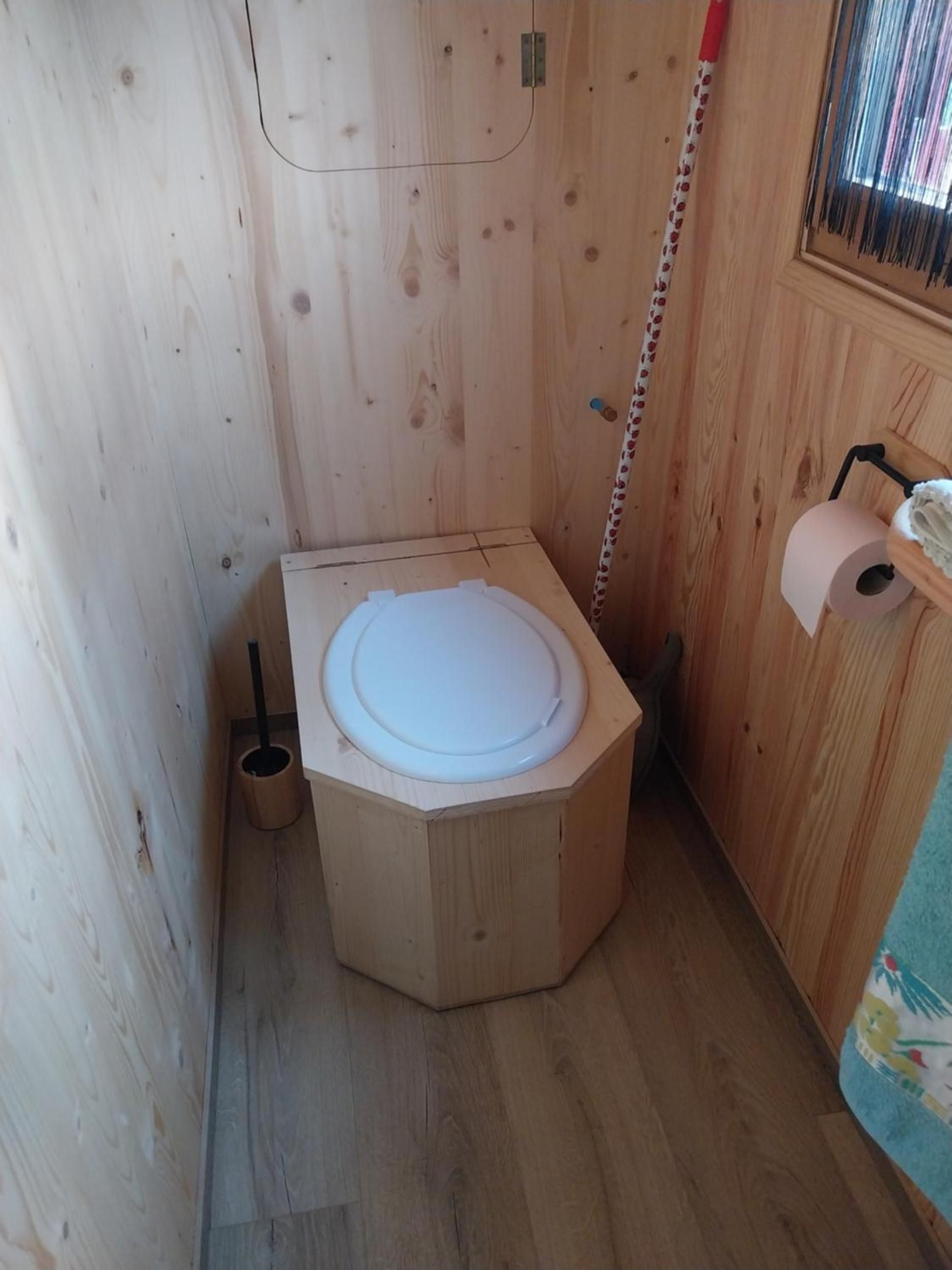 Un bagno compatto e ottagonale in legno, con un rotolo di carta igienica sulla destra.