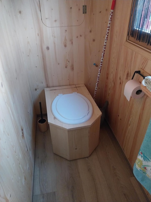 En liten, åttakantig toalett av trä, med en toalettpappersrulle placerad till höger.