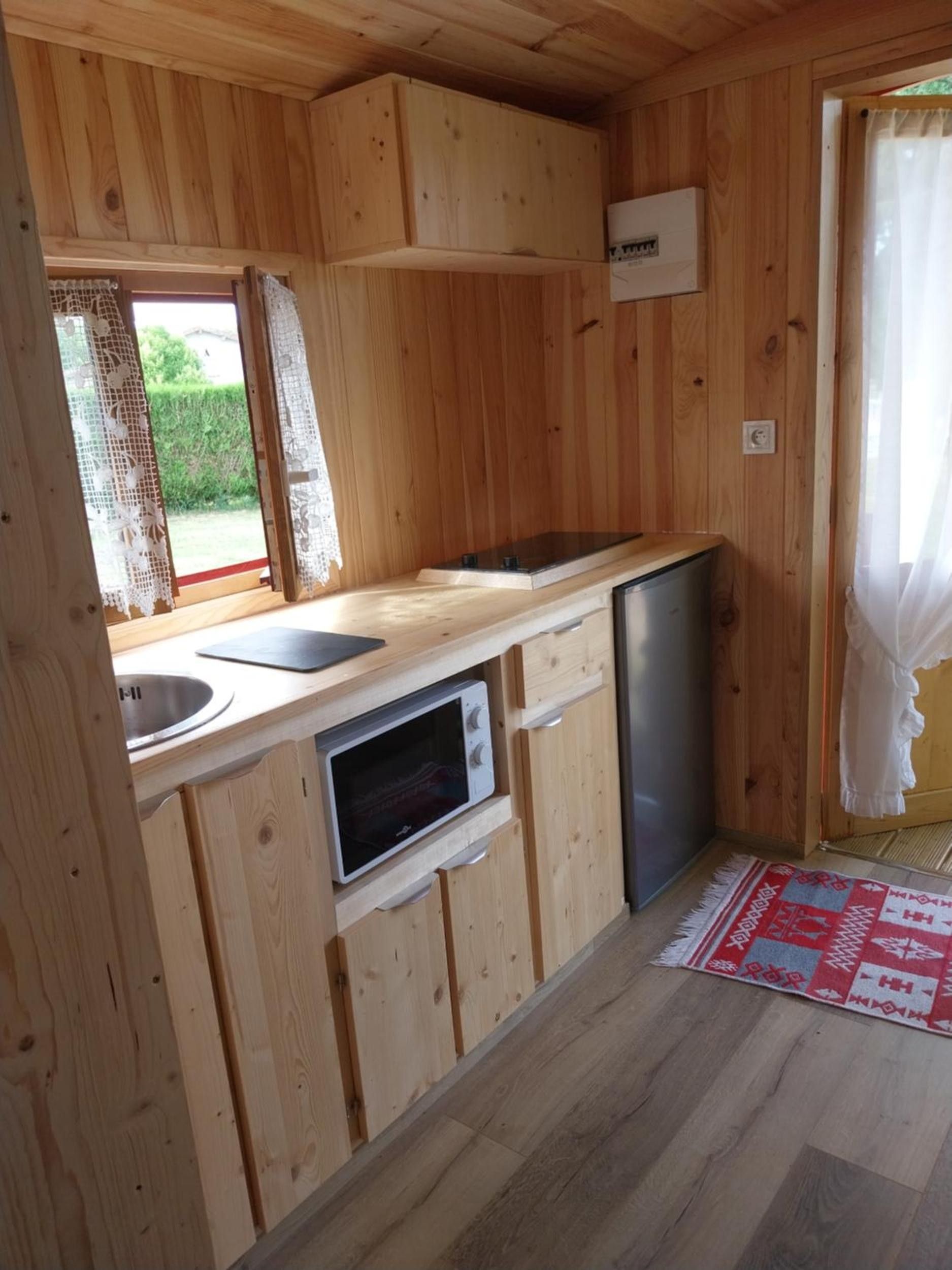 Eine kompakte Küche mit Holzschränken, einer Mikrowelle, einem Spülbecken und einem kleinen Kühlschrank.