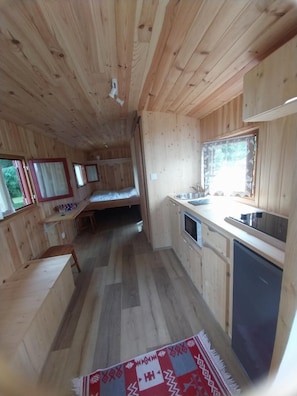 Eine kleine Holzhütte mit Küchenzeile, einem Einzelbett und einem fenster mit Vorhängen.