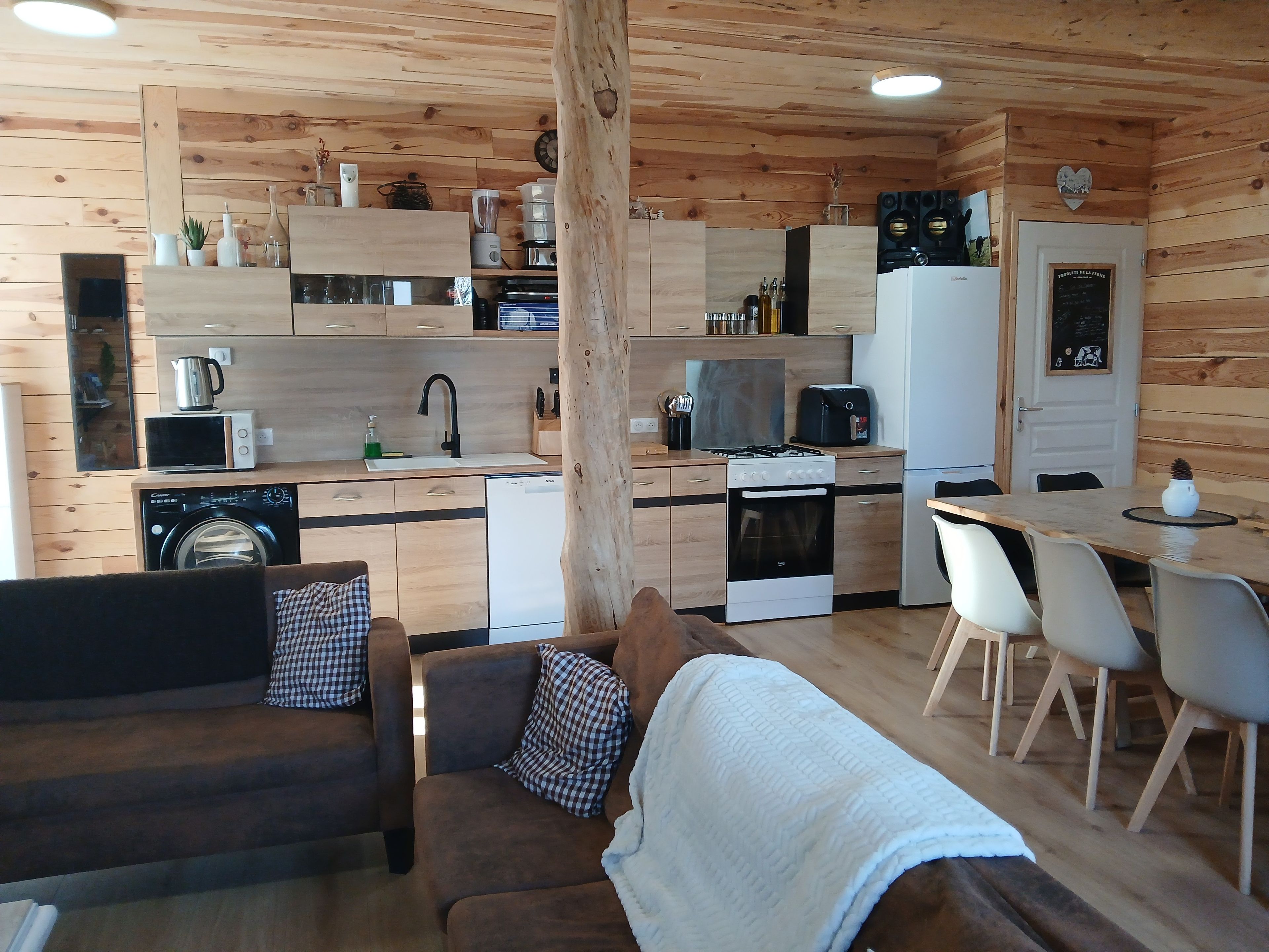 L’intérieur chaleureux d’un chalet, avec un revêtement en bois, une petite cuisine, un coin repas et un espace de vie comprenant un canapé et une couverture.