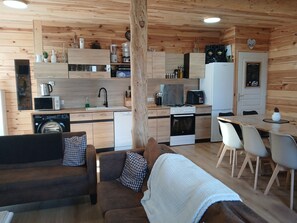L’intérieur chaleureux d’un chalet, avec un revêtement en bois, une petite cuisine, un coin repas et un espace de vie comprenant un canapé et une couverture.