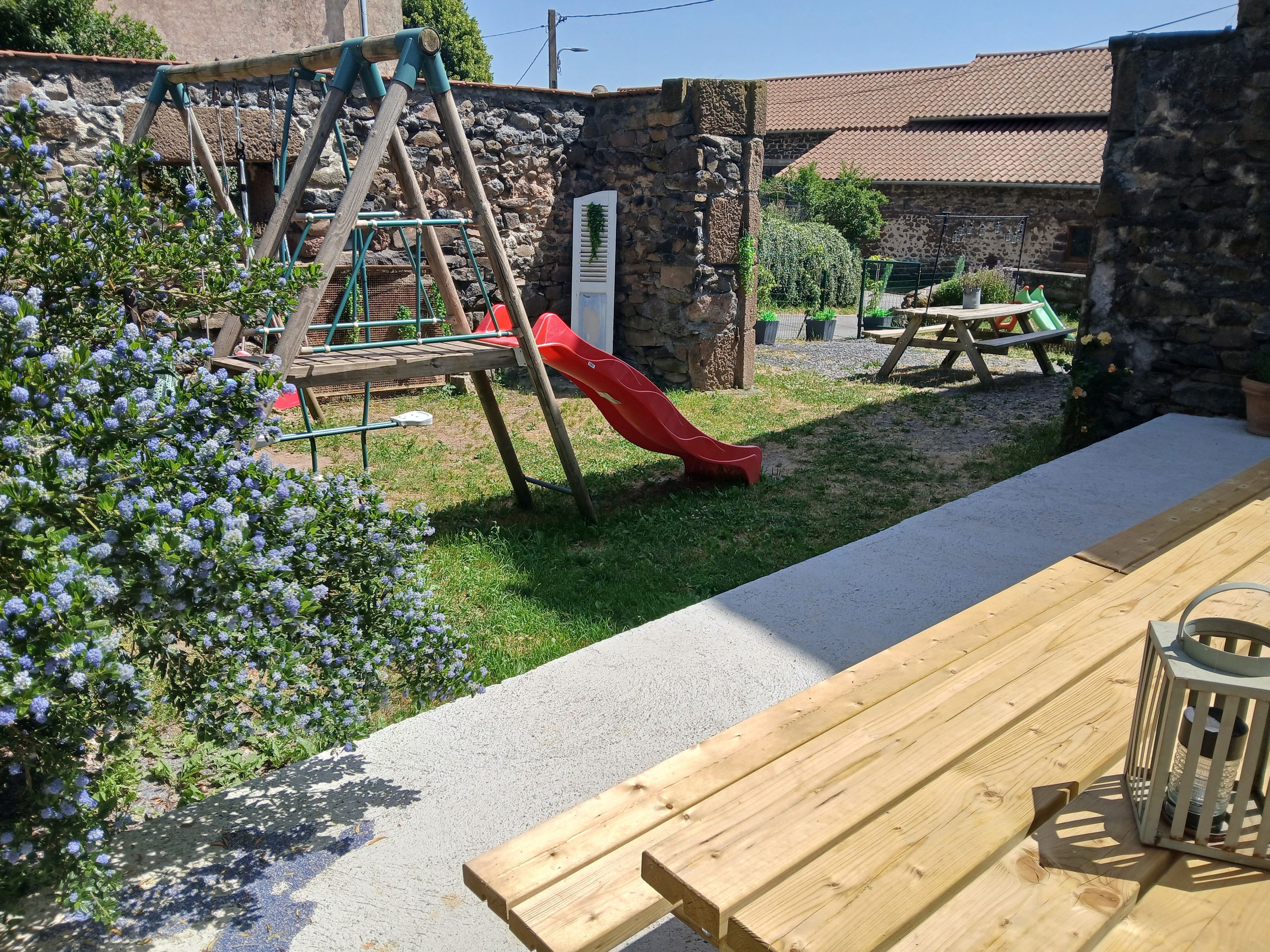 Un banc en bois et un toboggan rouge dans un jardin, avec un mur en pierre et de la verdure.