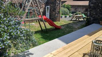 Un banc en bois et un toboggan rouge dans un jardin, avec un mur en pierre et de la verdure.