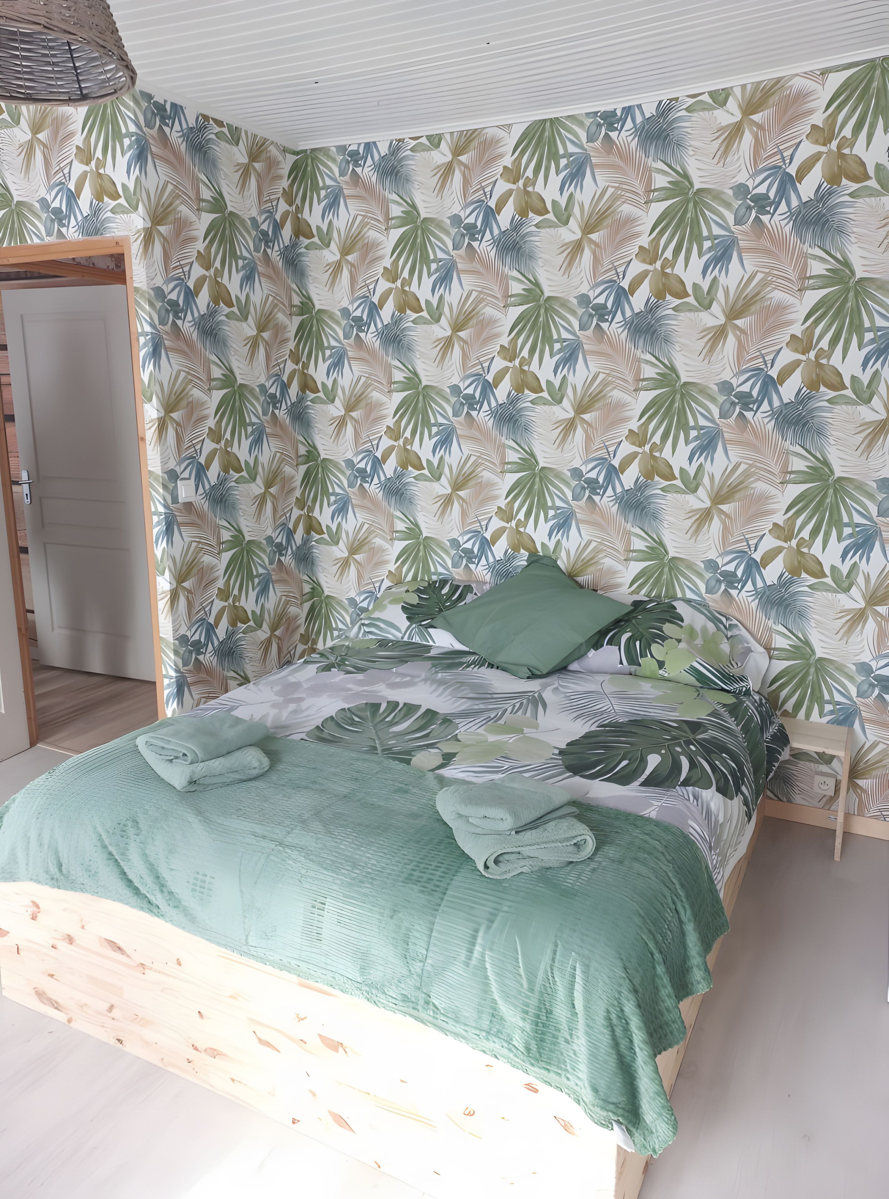 Une chambre à coucher avec un lit, une tête de lit en bois et un mur orné d’un motif de feuilles tropicales.