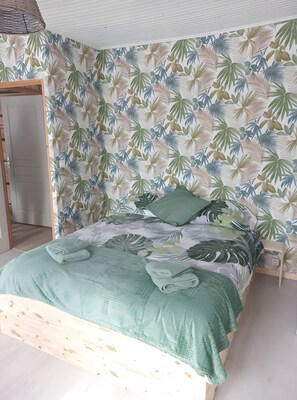 Une chambre à coucher avec un lit, une tête de lit en bois et un mur orné d’un motif de feuilles tropicales.