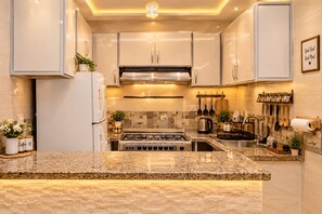 A modern kitchen with granite countertops, stainless steel appliances, and a variety of utensils hanging on the wall. - Arkan Egyptian Museum Hotel (Giza)