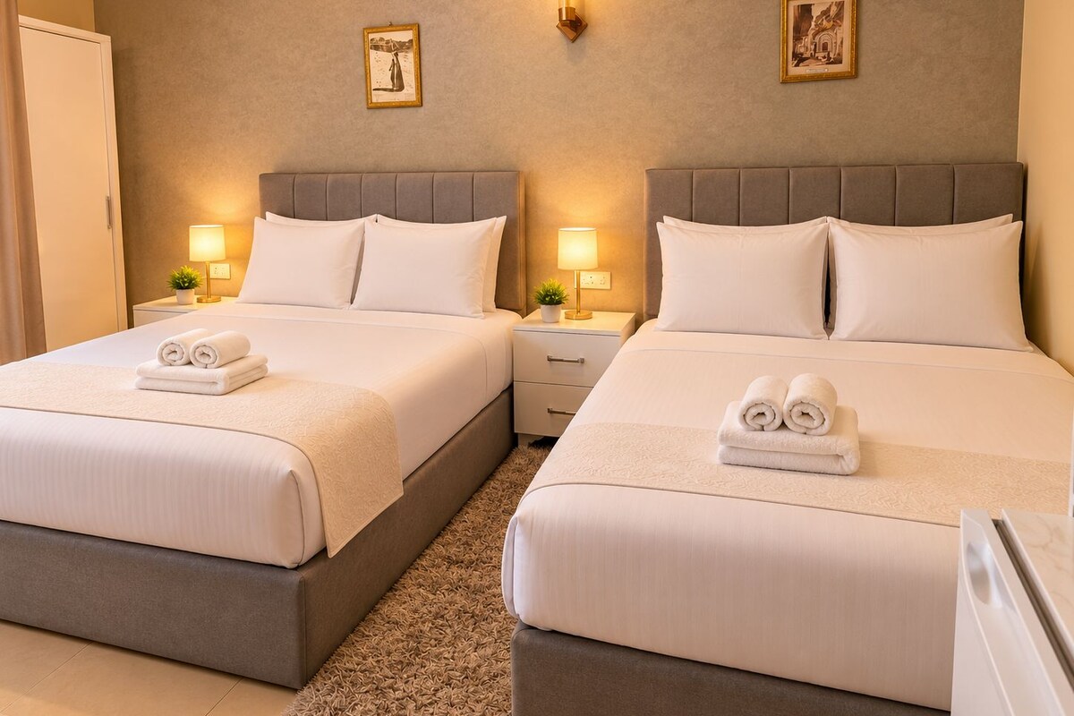 A hotel room with two beds, each with a headboard, bedside tables, lamps, and towels.