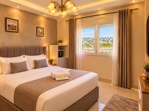 A hotel room with a large bed, a desk, a view of a building, and a chandelier. - Arkan Egyptian Museum Hotel (Giza)