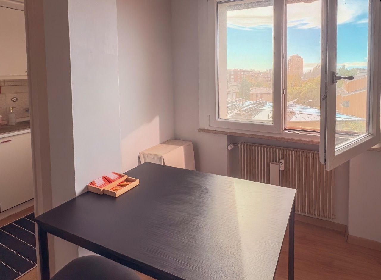 A room with a black table, a radiator, and a window with a view of buildings.