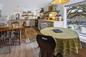 A cozy kitchen with a dining area, wooden furniture, and a large window offering a view of trees. - Mcfoy Ranch 20 Acres, Sleeps 8 (Wimberley)