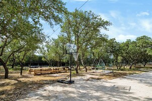 A basketball court with a wooden bench and chairs, surrounded by trees.