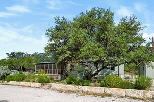 A house with a large tree in front, a small shed, and a paved area.