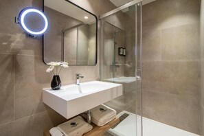 Un bagno moderno con cabina doccia in vetro, un lavandino bianco con specchio soprastante e un vaso con fiori bianchi.