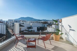 Una terrazza sul tetto con due sedie e un tavolo, con vista su uno skyline urbano e una montagna all'orizzonte.