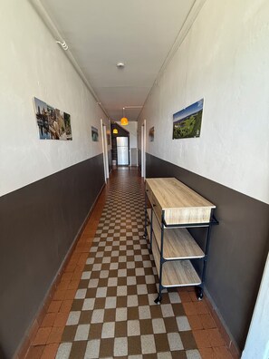 Un pasillo con piso a cuadros, una mesa con cajones y dos lámparas colgantes.