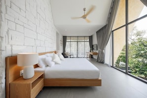 A modern bedroom with a large bed, a bedside table with a lamp, a ceiling fan, and a view of greenery through large windows. - SENDORO RETREAT (Thanh pho Ho Chi Minh)
