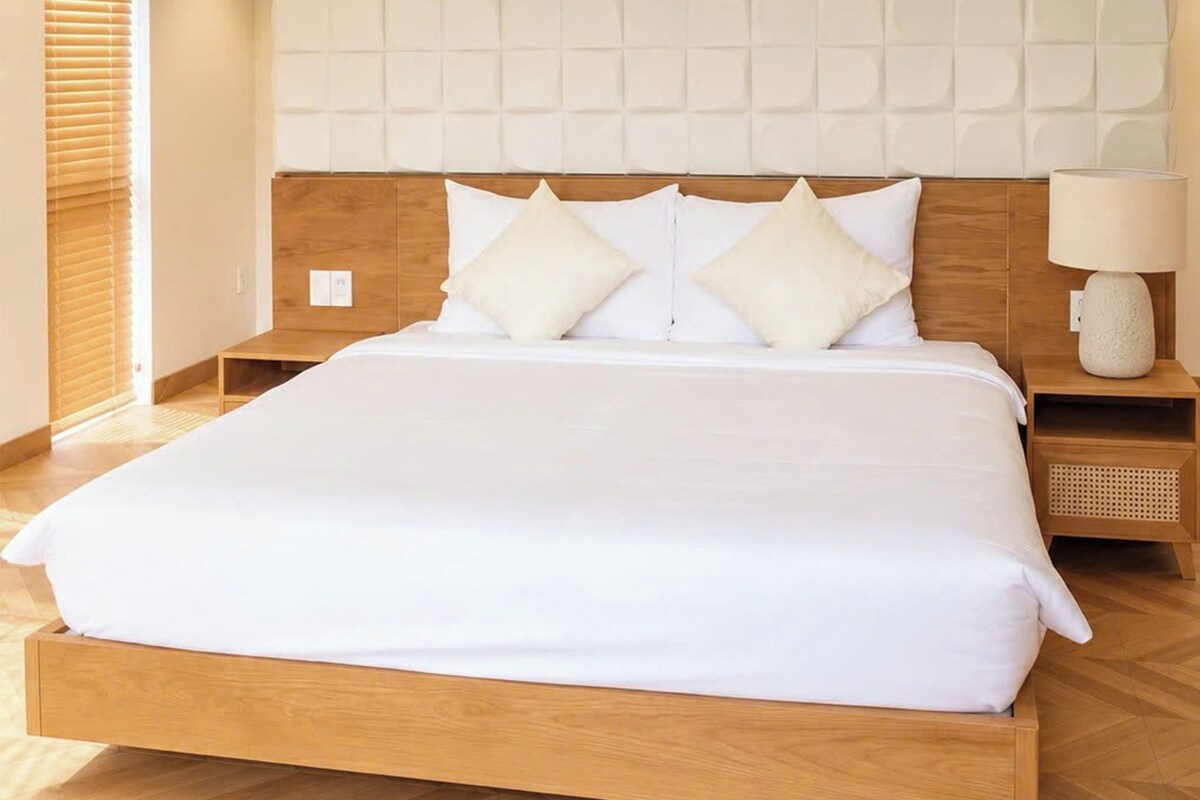 A hotel room with a wooden bed, white bedding, and a nightstand with a lamp.
