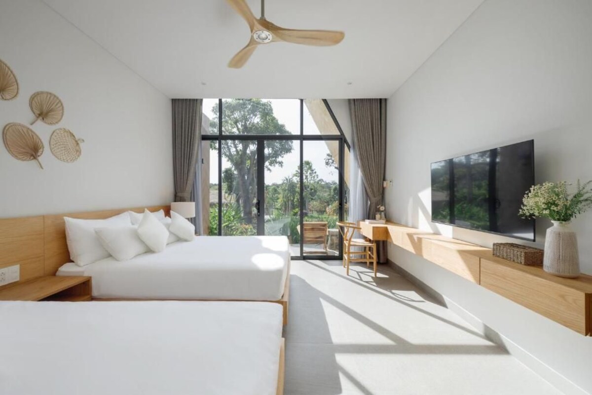 A modern bedroom with two beds, a desk, and a TV.
