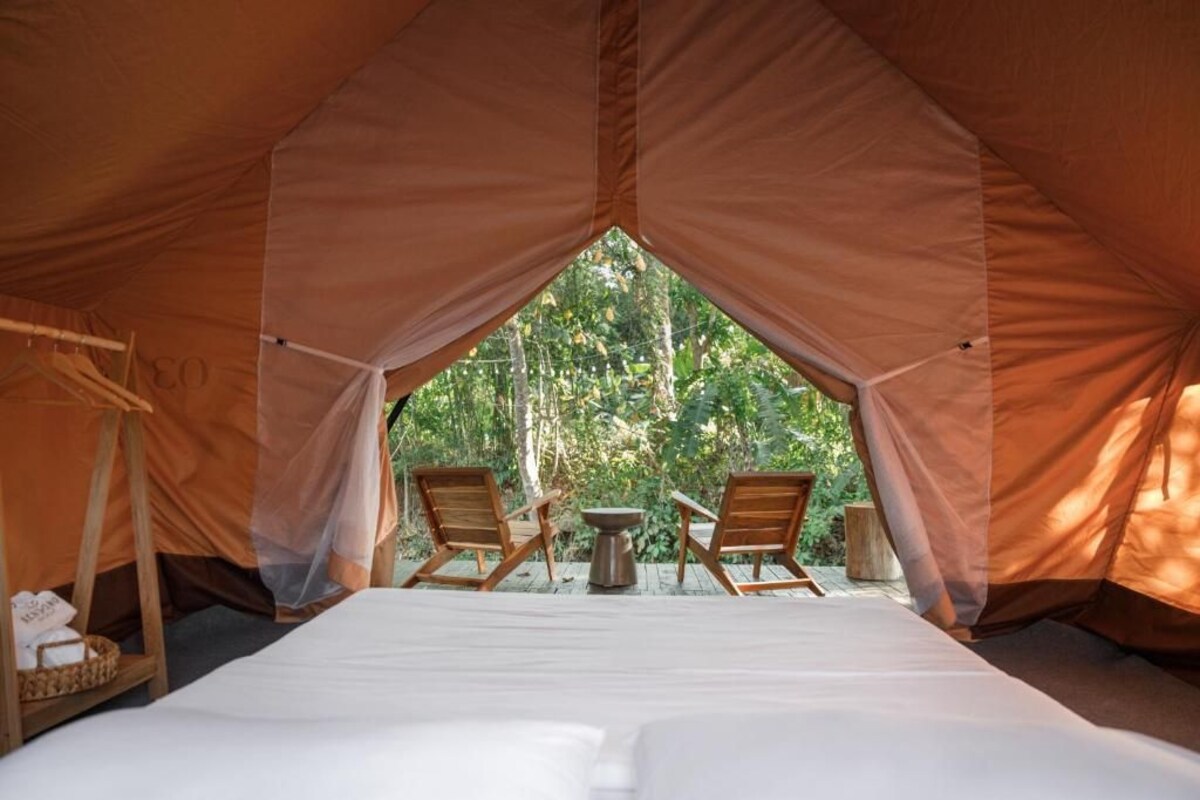 A tented accommodation with a bed, two wooden chairs, and a small table.