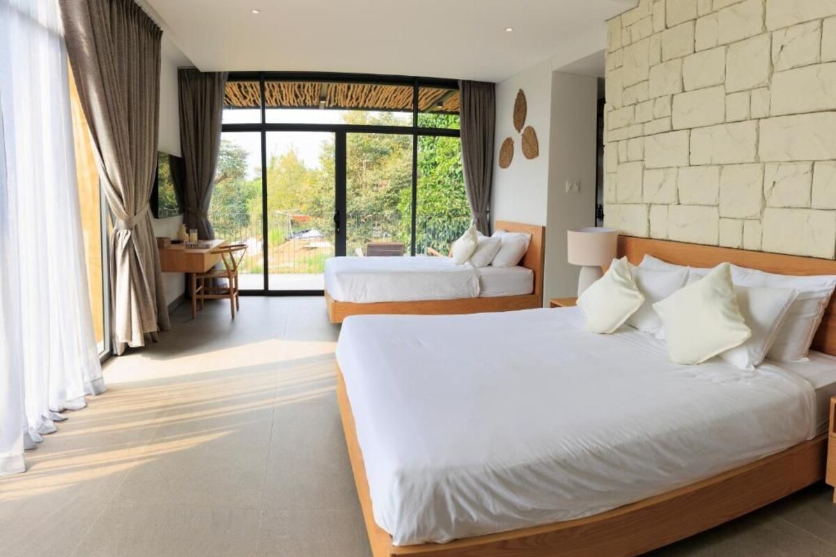A hotel room with two beds, a desk, and a large window.