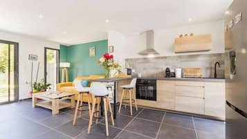 Une cuisine moderne avec un îlot central, des tabourets en bois, une table à manger et un canapé.
