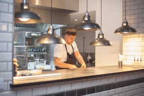 Um chef trabalhando em uma cozinha moderna, com iluminação pendente e eletrodomésticos de aço inoxidável.