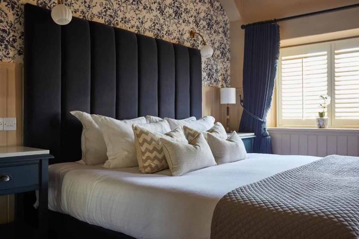 Quarto com uma cama grande, mesa de cabeceira, luminária e janela com cortinas.