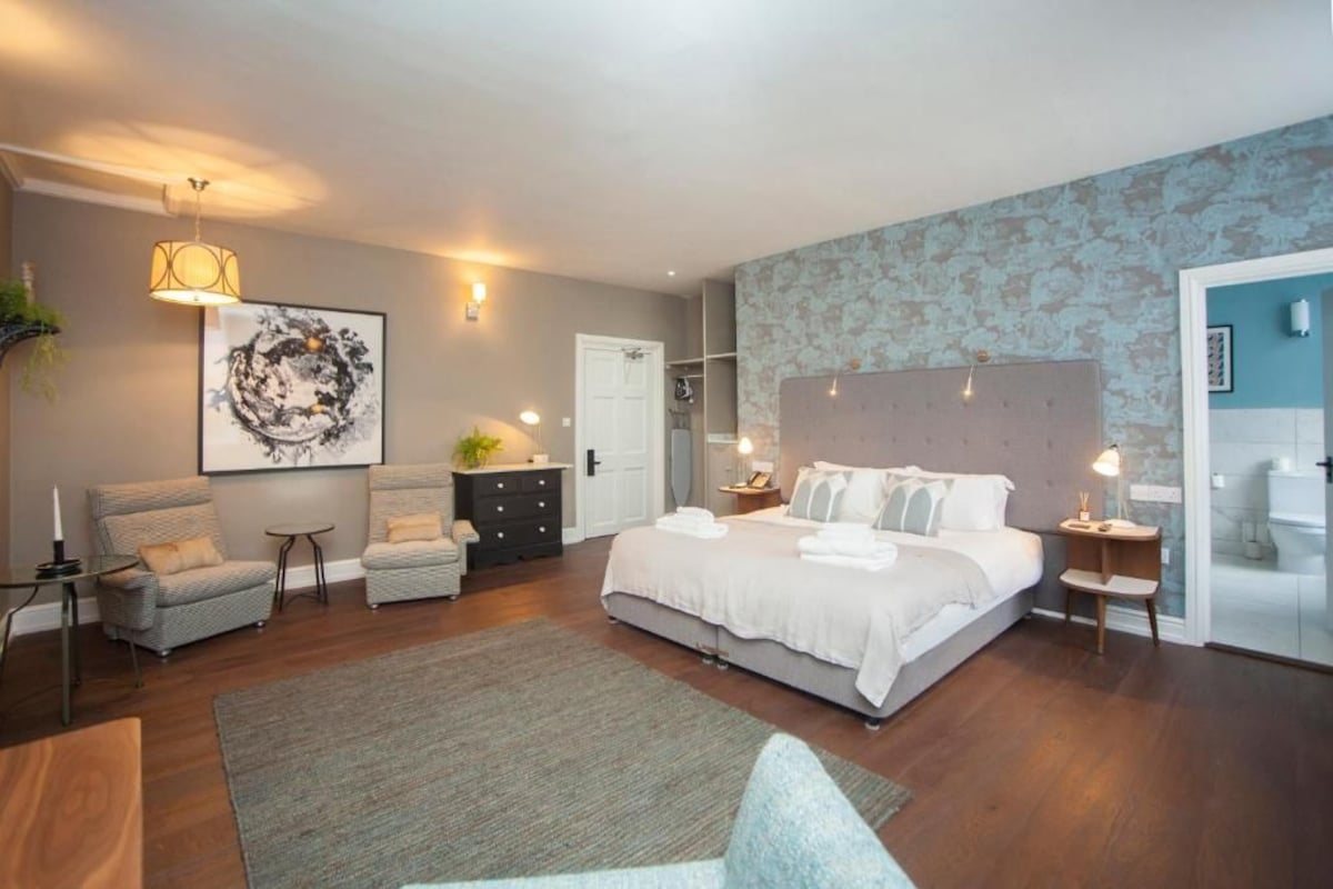 Quarto moderno com uma cama grande, duas poltronas, um penteado e uma obra de arte na parede.