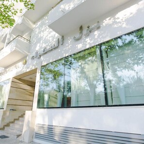 Un bâtiment doté d’une grande fenêtre en verre qui reflète les arbres, d’un escalier et d’une façade blanche.