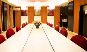 Une salle de conférence avec une longue table, des chaises rouges et un vase rempli de fleurs.