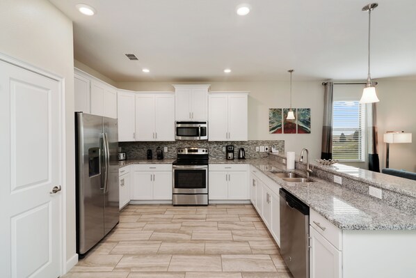 A modern kitchen with white cabinets, stainless steel appliances, granite countertops, and a herringbone floor pattern. - Valley Retreat. Spacious 9-bedroom house in peaceful ChampionsGate with AC (ChampionsGate)