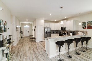 A modern kitchen with a central island, bar stools, stainless steel appliances, and a backsplash. - Valley Retreat. Spacious 9-bedroom house in peaceful ChampionsGate with AC (ChampionsGate)