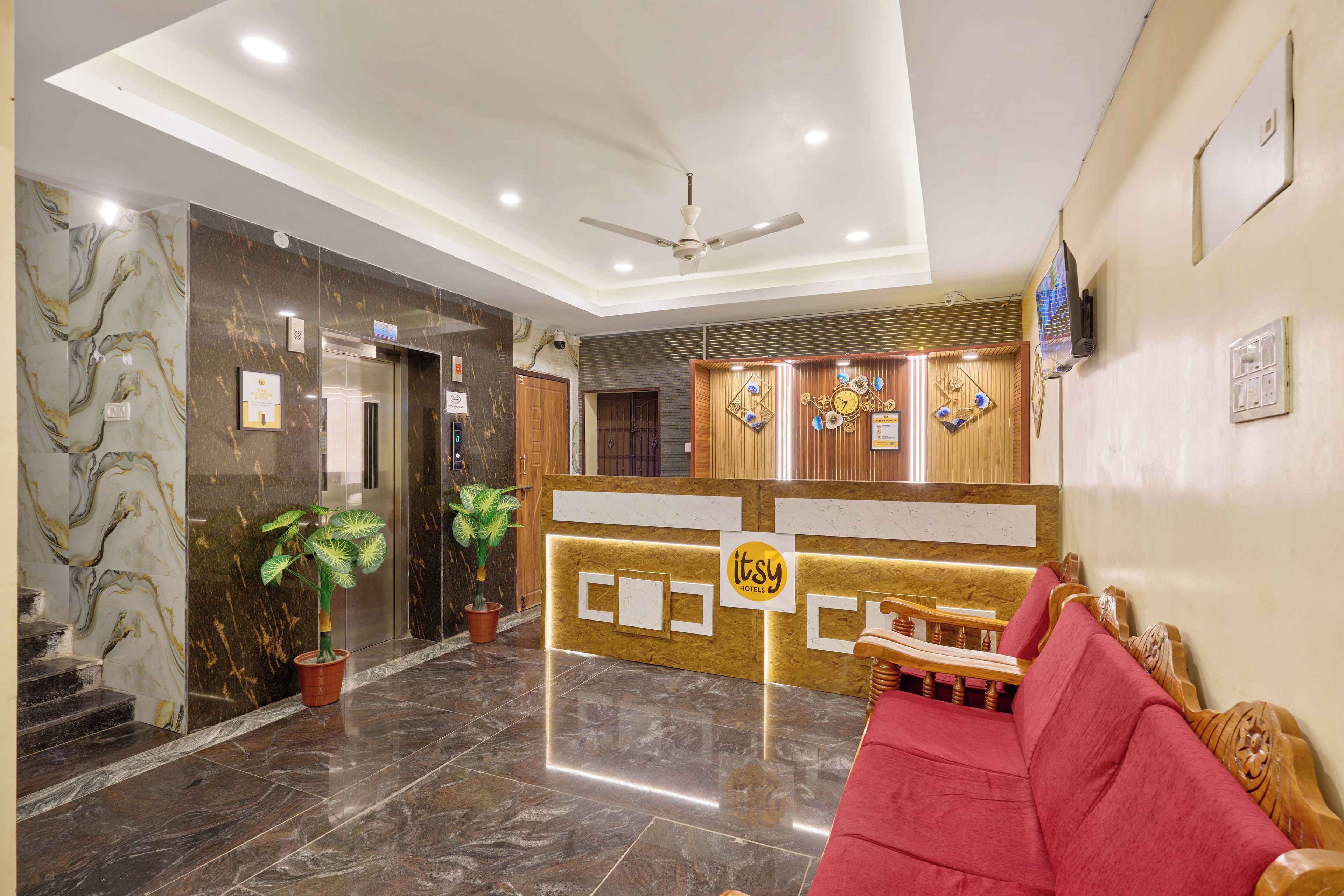 A hotel reception area with a marble floor, a reception desk, a red sofa, and a ceiling fan.