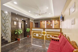 A hotel reception area with a marble floor, a reception desk, a red sofa, and a ceiling fan. - Itsy Hotels Mount Oasis, Tiruvannamalai (Tiruvannamalai)
