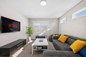A modern living room with a flat-screen TV, a coffee table, a sofa, and a potted plant. - 3BR Main & Upper Floor in Airdrie | Sleeps 9 | Canal View (Airdrie)