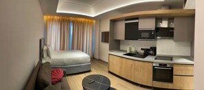 Une chambre d’hôtel moderne dotée d’une cuisine au design incurvé, d’un canapé, d’une table à manger et d’un grand lit.