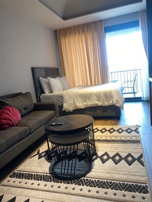 A hotel room with a bed, a sofa, a small table, and a patterned rug. - Zen Cantonments Studio · WiFi, Pool, Gym & Balcony (Accra)