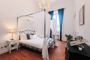 A four-poster bed with white bedding, a bedside table with a lamp, and a small potted plant on the floor. - New Listing (Roma)