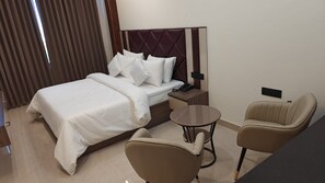Une chambre d’hôtel avec un lit, une table de chevet, une lampe et deux chaises.
