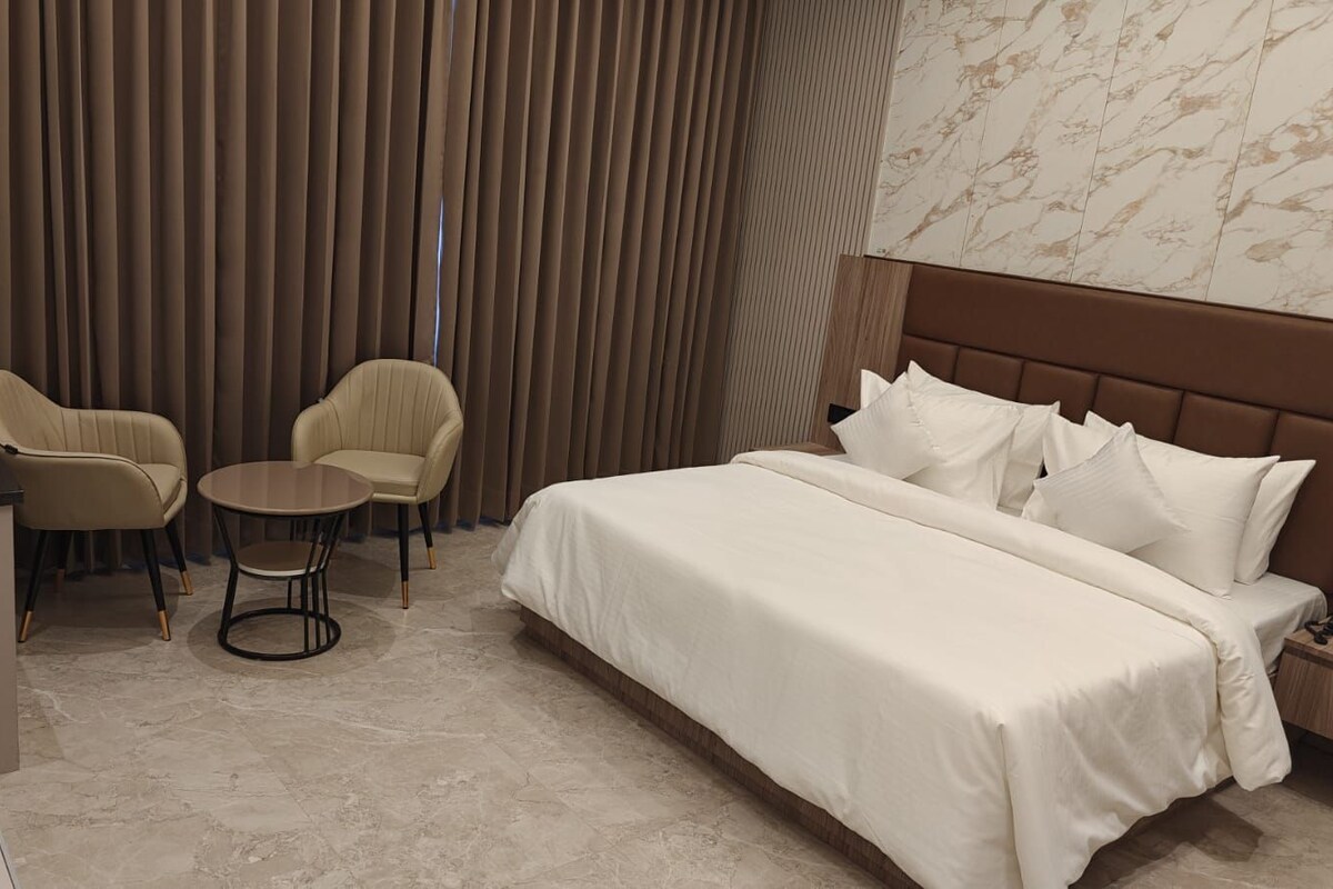 Une chambre d’hôtel avec un lit, deux chaises, une petite table et une table de chevet avec un téléphone.